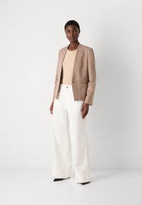 Beige blazer with slim lapels and a small front pocket, paired with white wide-leg trousers and black pointed heels. Smooth fabric texture.