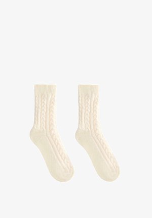 Pletené krémové ponožky s vrkočovým vzorom po stranách a rebrovaným lemom pre zvýšenú textúru a pevné priliehanie.