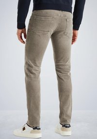 Jeans casual de corte slim en color caqui con múltiples bolsillos, detalles de costura y una textura suave, combinados con zapatillas blancas con un acento negro.