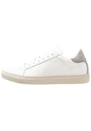 Biały niski sneaker z beżową podeszwą i szarą zamszową naszywką na pięcie, z białymi sznurowadłami i górną częścią z gładkiej skóry.