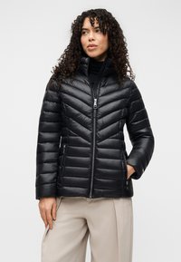 Μαύρο μπουφάν puffer με σχεδιασμό κεντήματος σε σχήμα βέλους, ψηλό γιακά, εμπρόσθιο φερμουάρ και πλαϊνές τσέπες. Λείο υφή και ελαφριά εμφάνιση.