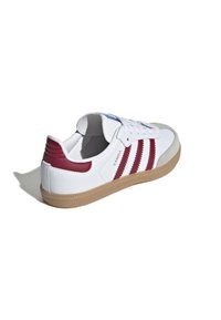 Baskets en cuir blanc avec des rayures bordeaux, des accents en daim gris et une semelle en caoutchouc gomme. Logo "Samba" sur le côté près du talon.