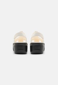 White and beige slide sandals with a thick black textured sole and adjustable straps, featuring an open design for ventilation.