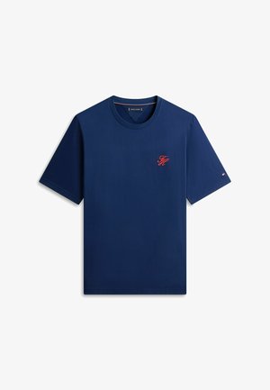 Camiseta de manga corta azul marino con cuello redondo, pequeño monograma rojo "FH" en el pecho y diminuto logo de bandera en la manga izquierda.