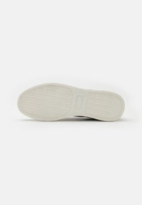 Semelle de chaussure en caoutchouc blanc avec une surface texturée et à motifs, présentant une forme lisse et arrondie avec un accent rectangulaire au centre.