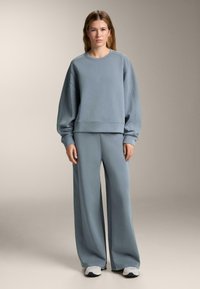 Svetlo modrý oversized sveter s rebrovanými manžetami a zodpovedajúcimi širokými nohavicami, vyrobený z mäkkého materiálu s hladkou textúrou. Neformálny dizajn.