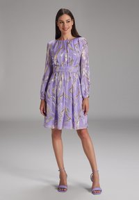 Robe lavande avec des manches longues, motif tourbillonnant doré, taille cintrée et jupe fluide. Assortie à des talons lavande.