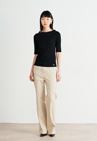 Svart avkortet topp med korte ermer, kombinert med beige brede bukser. Glatt tekstur, minimalistisk design, subtilt preg på skjorten.