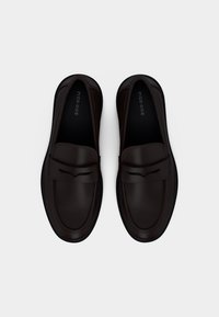 Ζευγάρι σκούρα καφέ δερμάτινα loafers χωρίς κορδόνια με στρογγυλεμένες μύτες και λιτή διακόσμηση, εμφανιζόμενα από πάνω σε λευκό φόντο.