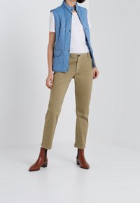 Hellblau gesteppte Weste, weißes T-Shirt und beige Chinos, kombiniert mit braunen Knöchelstiefeln. Auffällige Details sind Druckknopfverschlüsse und Taschen.