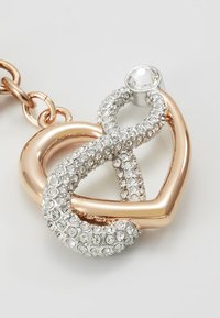 Pendente in metallo rosa e argento a forma di infinito, adornato con strass trasparenti, con un singolo cristallo più grande come accento.