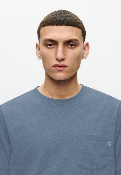 Blå crewneck sweatshirt tillverkad av mjukt tyg. Har en bröstficka på vänster sida med en subtil logotagg. Slät textur med avslappnad passform.