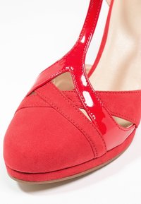 Chaussure à talon haut pour femme rouge avec bout en daim et lanières en cuir verni brillant, gros plan sur les détails avant et latéraux.