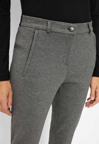 Pantaloni grigi in tessuto morbido, caratterizzati da un davanti piatto con chiusura a bottone, tasche laterali inclinate e una forma sagomata.