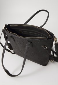 Black synthetic tote bag with embossed logo pattern, dual top handles, zippered closure, and interior compartments. Gold-tone hardware accents.