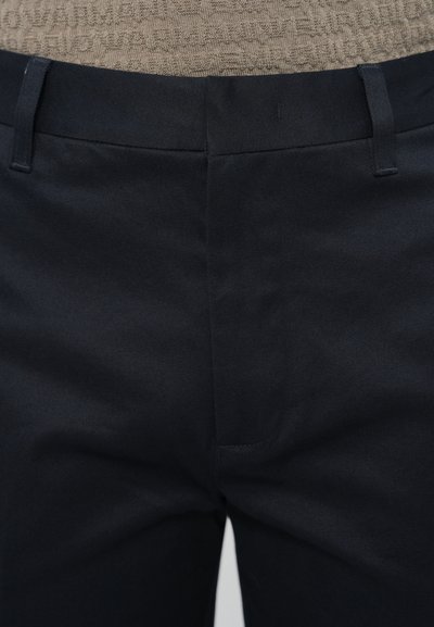 Granatowe spodnie wykonane z gładkiej tkaniny, z płaskim przodem, szlufkami na pasek i minimalnymi detalami szwów.