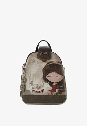 Sac à dos en similicuir marron avec une illustration de fille dessin animé, des accents dorés et un charm décoratif. Il dispose d'une fermeture éclair et d'une poignée supérieure.