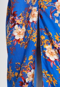 Tela floral azul con flores brillantes en amarillo y rojo, con un detalle de abertura. Textura suave, adecuada para vestidos o faldas.