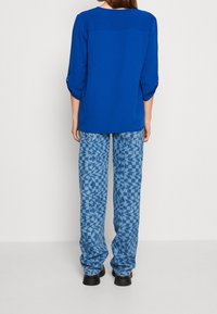 Blauwe textuur top met driekwart mouwen, gecombineerd met loszittende blauwe gebloemde broeken. Opvallend geometrisch ontwerp door de hele broek.