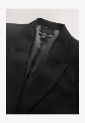 Čierne sako so saténovým povrchom, ostrými goliermi a jedným predným vreckom. Má značkovú vnútornú etiketu. Hladká textúra.
