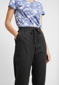 Szare spodnie treningowe z elastycznym pasem, szczegółami ze sznureczkiem i bocznymi kieszeniami, zestawione z niebieską koszulą z krótkim rękawem w stylu tie-dye.