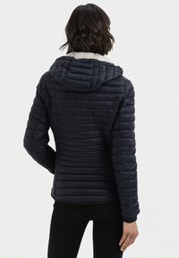 Navy puffer jacket with a hood, featuring quilted texture, a contrasting light-colored lining, and elastic cuffs. Designed for warmth and comfort.