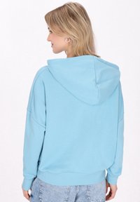 Sudadera con capucha de color azul claro, de corte relajado, con hombros caídos, puños y dobladillo acanalados. Tejido suave con una textura lisa.