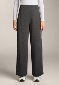 Široké nohavice z tmavošedej rebrovanej látky, s vysokým pásom a čistými líniami, skombinované s bielym vrchom s dlhým rukávom a bielymi teniskami.