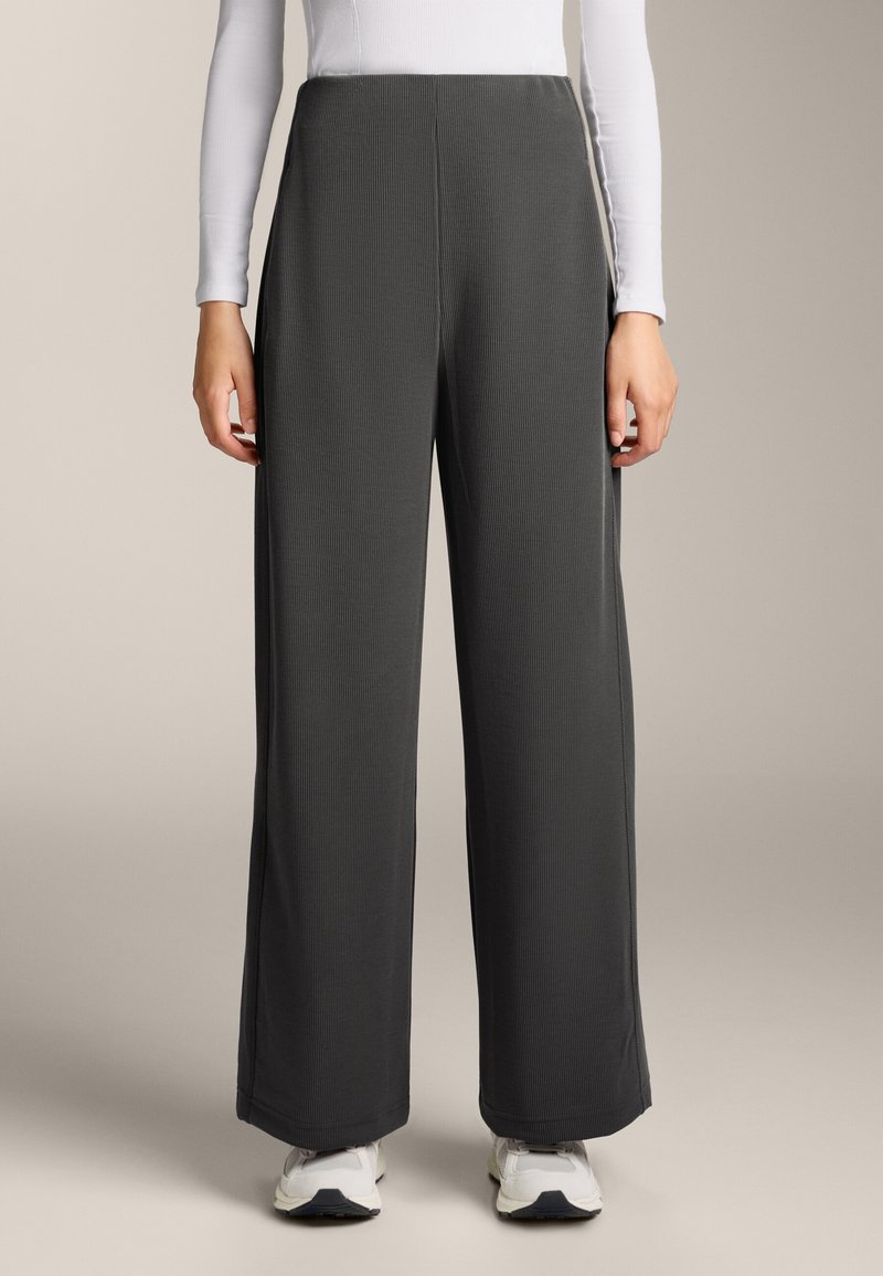 Široké nohavice z tmavošedej rebrovanej látky, s vysokým pásom a čistými líniami, skombinované s bielym vrchom s dlhým rukávom a bielymi teniskami.