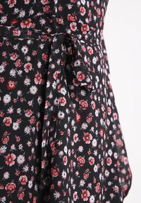 Tela negra con un pequeño estampado floral en rojo y blanco, que cuenta con un cinturón atado en la cintura.