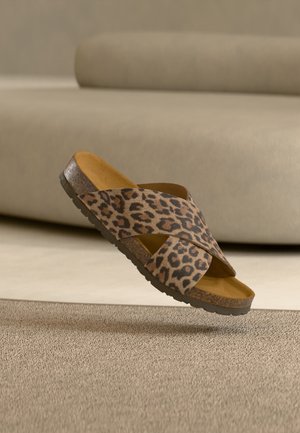 Leopardimustriga libisev sandaal krussis rihmade ja tekstuurse tallaga, paikneb beeži vaiba ja diivani taustal.