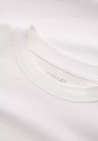 Camiseta blanca de cuello redondo en suave algodón, con un diseño simple y una etiqueta sutil "LEVEL UP" en el interior del cuello.