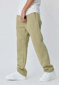 Joggers ajustés vert olive en tissu doux, avec des coutures latérales et des chevilles resserrées, associés à des baskets blanches.
