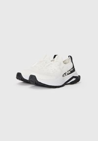 Zapatillas deportivas blancas con acentos de suela negra y marca. Presentan una parte superior texturizada, cierre de cordones y un collar acolchado para mayor soporte.