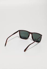 Ochelari de soare din scoică cu lentile întunecate, ramă rectangulară și brațe subțiri cu vârfuri curbate. Suprafață texturată cu finisaj lucios.