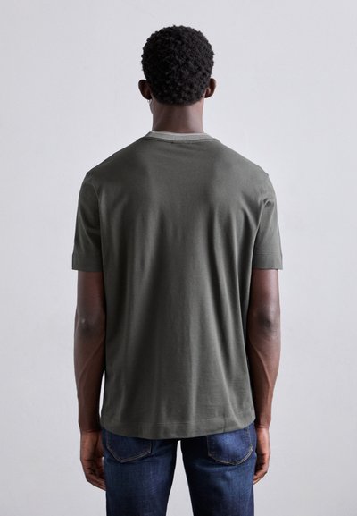 T-shirt vert olive à manches courtes en coton, avec un col rond et une texture douce, associé à un jean en denim bleu.