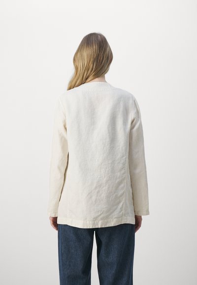 Veste en lin beige clair à manches longues, avec un col rond et une coupe droite, vue de l'arrière sur un fond uni.