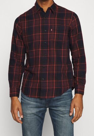 Chemise à carreaux à boutons en marine et rouge, fabriquée dans un tissu à la texture douce. Elle est dotée de manches longues et d'une poche poitrine.