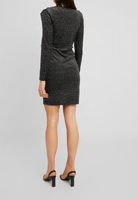 Svart långärmad klänning med en figursydd form, har ett prickigt mönster, slät textur, knälång, bärs med svarta högklackade sandaler.