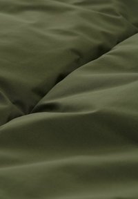 Grønt stof med en glat tekstur, der har bløde folder og rynker, hvilket indikerer et materiale til sengetøj eller polstring.