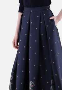 Marineblauer Rock mit goldenen, runden Mustern, Falten und seitlichen Taschen. Verfügt über bestickte Hundedesigns am Saum. Glattes, texturiertes Gewebe.