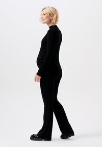 Haut à manches longues noir côtelé associé à un pantalon évasé assorti. Le tissu est extensible et lisse, conçu pour une silhouette ajustée.