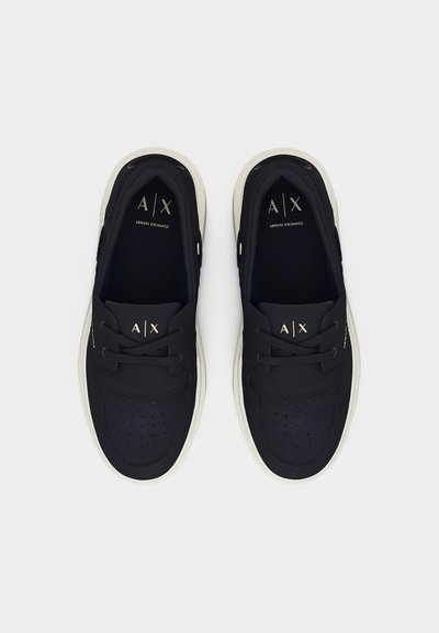 Paire de baskets noires Armani Exchange avec semelles blanches, style à lacets et zone perforée à l'avant, vue de dessus.