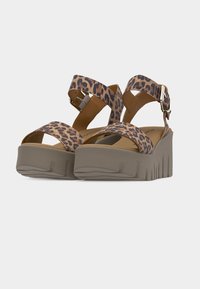 Paire de sandales compensées avec semelles épaisses beiges et lanières imprimé léopard, avec boucles à la cheville et orteils ouverts.
