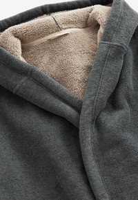 Huppari harmaasta fleece-materiaalista, jossa on pehmeä beige sisus. Siinä on huputettu kaulus, ja se on valmistettu rakenteellisesta, lämpimästä kankaasta mukavuutta varten.
