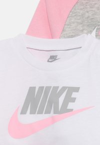 Tricou Nike din material alb cu un logo gri și un design swoosh roz. Tricoul are guler rotund și textură netedă.