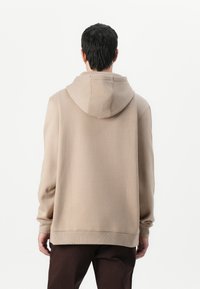 Un hoodie beige en tissu doux, doté d'une capuche avec cordon de serrage et de manches côtelées, conçu avec une coupe décontractée et une texture unie.