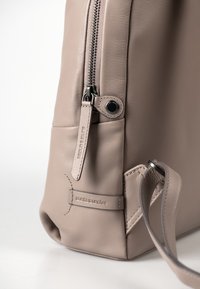 Borsa in pelle di un taupe chiaro con una superficie liscia. Presenta una cerniera prominente, un'etichetta con logo e una tracolla stretta con un accento in metallo.