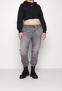 Sudadera corta negra con capucha y cordón, combinada con joggers gris ajustados que tienen una cinturilla y puños elásticos. Botas de combate negras.