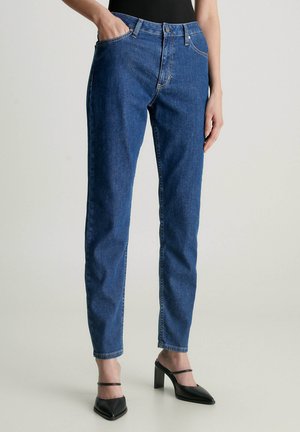 Jeans in denim blu a gamba dritta con vita alta, dotati di tasche frontali e chiusura a bottone, abbinati a décolleté nere a punta.